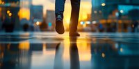 Person walking on wet reflective surface during golden sunset hour with urban bokeh lights creating mirror effect and atmospheric urban mood.