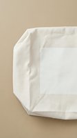 Folded white linen fabric with natural texture displayed against neutral beige background, showcasing organic cotton material suitable for textile design, home decor, and packaging mockups.