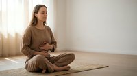 Pregnant woman in comfortable brown loungewear sitting cross-legged on yoga mat practicing mindful meditation in bright minimalist room for wellness.