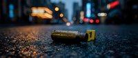 Crime scene evidence bullet casing with yellow marker on urban street at night with blurred city lights and traffic background for forensic investigation.