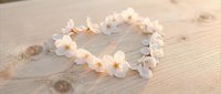 Delicate white flower crown lei arranged in heart shape on rustic wooden surface for wedding decoration, bridal accessories, romantic celebration events.
