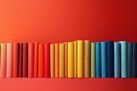 Row of colorful books arranged in rainbow spectrum order from pink to blue standing against vibrant red wall background, creating minimalist gradient composition.