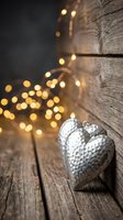 Silver heart ornament on rustic wooden surface with warm bokeh lights creating cozy holiday atmosphere for seasonal decorating and festive celebrations.