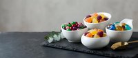 Colorful assorted candies and sweets displayed in white ceramic bowls on dark slate board for confectionery and dessert presentations.