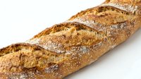 Freshly baked whole wheat baguette with crispy crust and diagonal scoring marks, isolated on white background for bakery, food, and culinary design projects.