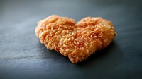 Crispy breaded chicken nugget arranged in heart shape on dark slate background, selective focus with soft bokeh, romantic fast food concept for Valentine's day.