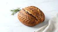 Rustic artisan sourdough bread loaf with golden crust on marble surface with rosemary sprig and linen cloth.