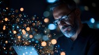 Mature bearded Caucasian businessman in glasses illuminated by glowing tablet screen with magical bokeh light effects in dark environment. Technology concept.