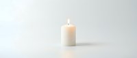 Single white pillar candle with a glowing flame isolated on a white background, evoking peace, remembrance, and calm ambiance.