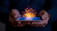 Glowing magical sparkles and light particles emerging from smartphone screen held in hands against dark background, representing digital transformation.