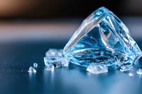 Sparkling ice crystals and fragments on dark blue surface with soft lighting create dramatic macro composition highlighting transparency and frozen texture.