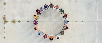 Diverse group of people standing in a circle holding hands viewed from above on concrete ground, representing unity, teamwork, community connection and collaboration.