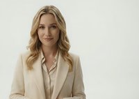 Professional blonde businesswoman in beige suit smiling confidently against neutral background for corporate presentations and marketing materials.