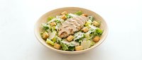 Grilled chicken Caesar salad in a bowl with romaine lettuce, croutons, and parmesan cheese on a white background.
