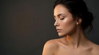Young brunette woman with natural makeup in profile view against dark background for beauty and skincare advertising campaigns.