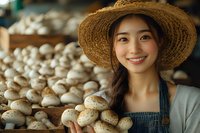 Young Asian female farmer in straw hat and apron smiling while holding fresh mushrooms at organic farm market, agricultural business concept.
