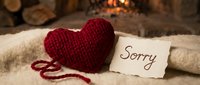 Knitted red heart with a sorry note on a cozy blanket by a warm fireplace, evoking apology, forgiveness, and reconciliation.