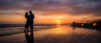 Romantic couple silhouette embracing on beach at sunset with golden sky and ocean waves reflecting on wet sand creating peaceful evening atmosphere.