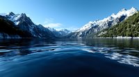 Majestic snow-capped mountain peaks reflect in dark blue rippling waters of alpine lake surrounded by evergreen forest under clear winter sky.