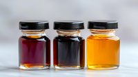 Small glass jars with colorful honey and syrup varieties lined up showing different natural sweetener options in amber, dark purple and burgundy tones.