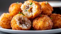 Crispy rice balls with mushroom filling garnished with fresh herbs on white plate. Close up view of golden brown Japanese style croquettes shows texture.