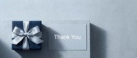 Elegant navy blue gift box with silver ribbon bow beside a thank you card on a light gray background, top view.