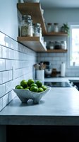 Fresh green limes in ceramic bowl on modern kitchen counter with white subway tile backsplash, wooden shelves, and storage jars. Bright, minimalist kitchen design for home decor and culinary content.