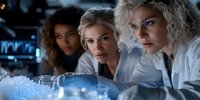Female scientists in white lab coats examining laboratory samples and research data in modern facility with specialized equipment and blue lighting atmosphere.