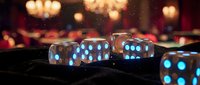 Close-up of translucent blue dice with glowing dots on dark surface, blurred warm lights in background, suitable for gaming, gambling, and entertainment concepts.