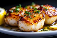 Pan seared sea scallops with caramelized golden crust garnished with fresh herbs and lemon on white plate against dark background, macro food photography.