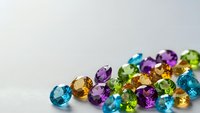 Collection of colorful faceted gemstones including emerald, sapphire, topaz, amethyst and citrine scattered on white background for jewelry design.