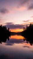 Serene lake at sunset with golden and purple sky reflecting on calm water, surrounded by silhouetted evergreen trees. Perfect for nature and travel projects.