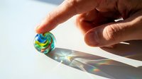 Caucasian male hand holding colorful lollipop candy against bright sunlight, creating rainbow light refraction effect for confectionery and sweet treat concepts.