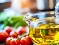 Fresh olive oil in glass jug with cherry tomatoes and herbs in background, macro food photography with selective focus for culinary and cooking concepts.