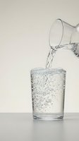Clear water being poured from glass pitcher into drinking glass with bubbles and splash on neutral background for health and hydration concepts.