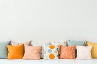 Decorative throw pillows in pastel and bright colors arranged in row against white wall, featuring polka dots and geometric patterns. Modern home decor styling.