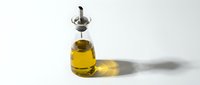 Glass bottle with golden olive oil and metal pourer on white background, casting a soft shadow. Minimalist food photography for culinary use.