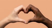 Two diverse hands forming heart shape symbol representing unity love friendship and racial harmony against warm peach background for social campaigns.
