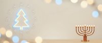 Festive holiday scene with glowing neon Christmas tree and golden menorah on wooden surface against warm beige wall with bokeh lights for seasonal celebrations.