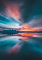 Dramatic sunset sky reflects on calm lake surface with mountain silhouettes, featuring vibrant coral pink clouds and deep turquoise waters creating mirror-like symmetry.