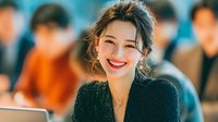 Young Asian businesswoman smiling confidently in modern office environment with colleagues in background for corporate and professional workplace concepts.
