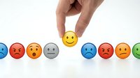 Male hand selecting yellow smiley face emoji among various colorful emotion icons on white background, representing customer satisfaction, feedback, and positive rating selection.