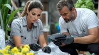 Caucasian male and female medical professionals in protective gloves reviewing patient data on tablet while working outdoors among plants and flowers.