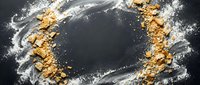 Golden granola and white flour scattered on dark surface with copy space for food styling and recipe content.