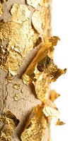 Luxurious gold leaf flakes applied to textured beige surface, creating elegant metallic accents. Perfect for luxury branding, wallpaper design, and premium packaging projects.