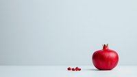 Vibrant red pomegranate and scattered seeds on light background with copy space, minimalist food composition for healthy eating and nutrition concepts.