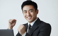 Successful Asian businessman celebrating achievement with raised fists, wearing formal suit against white background. Professional portrait for business concepts.