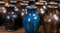 Rustic ceramic vases in deep blue and earthy brown tones with textured, weathered surfaces create artisanal display. Handcrafted pottery collection shows vintage patina finish.