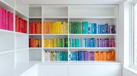 Modern white bookshelf with colorful books arranged by rainbow spectrum creating organized home library interior design for reading room decor.