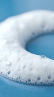 White foam bubbles floating on blue water surface creating abstract cleaning and hygiene concept for spa wellness and bathroom products.